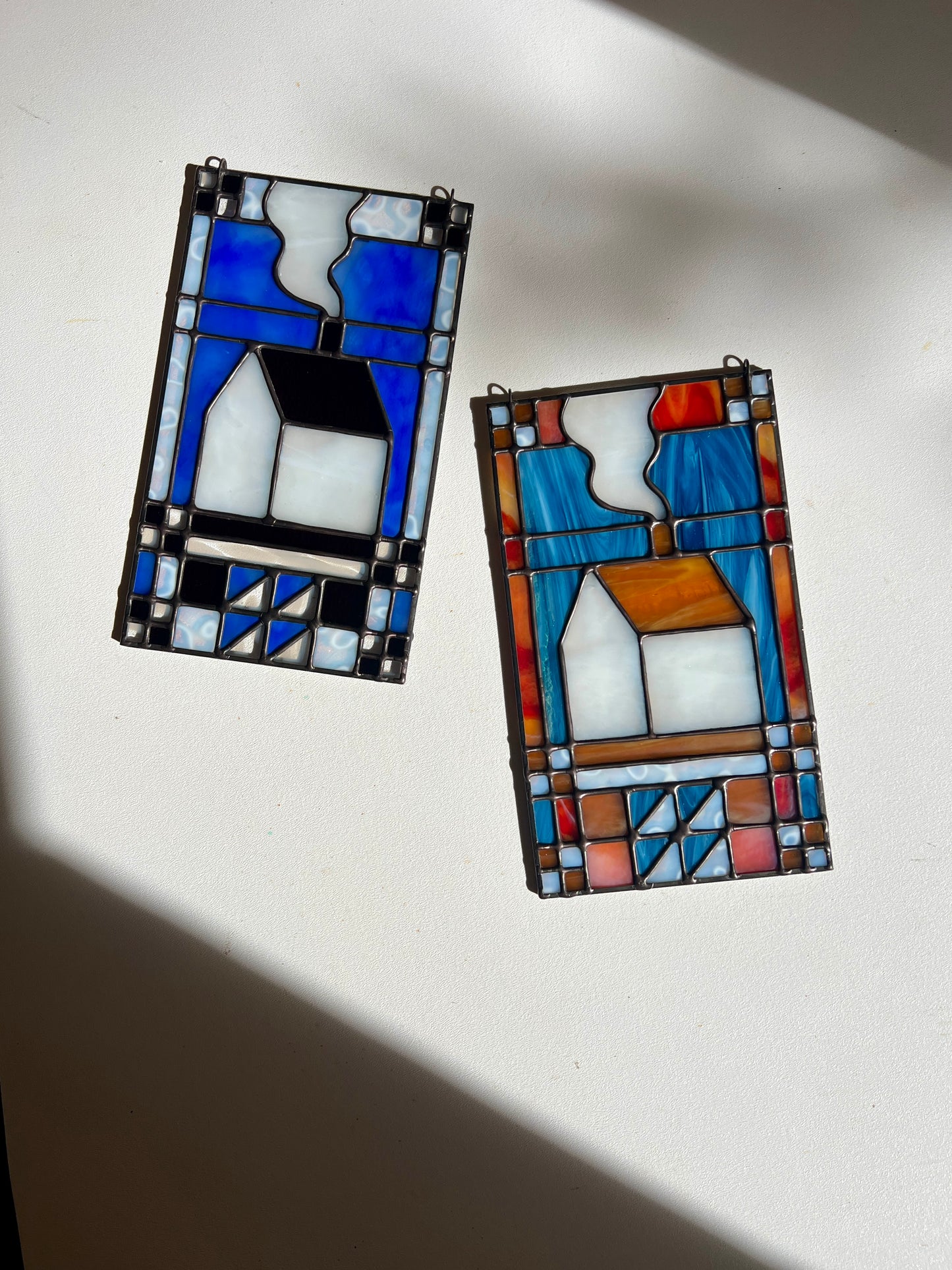 Two textile inspired stained glass panels laying on a white surface with bright sunlight cast across them