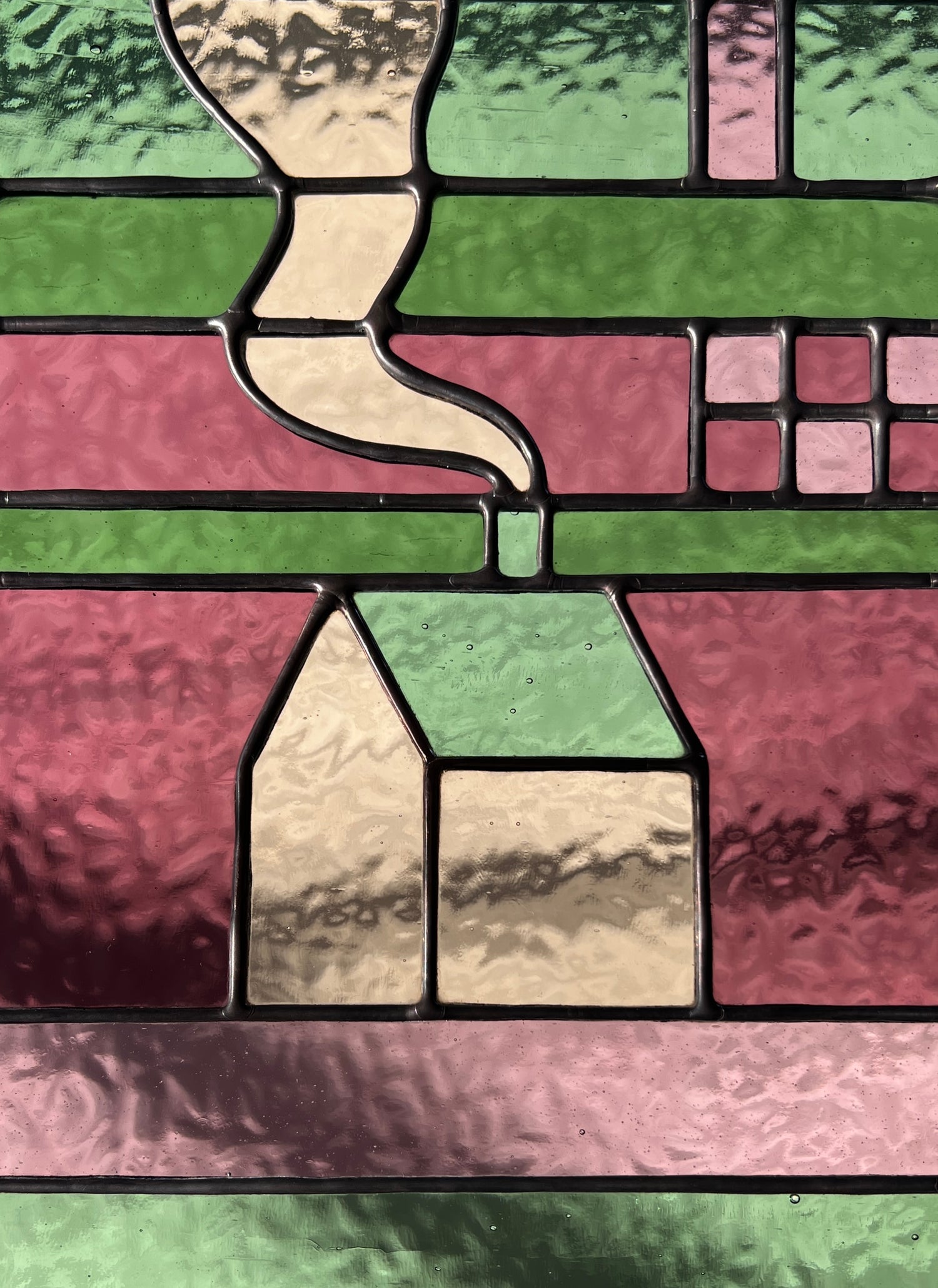 Close-up of a stained glass window with geometric patterns, in shades of pink and green glass