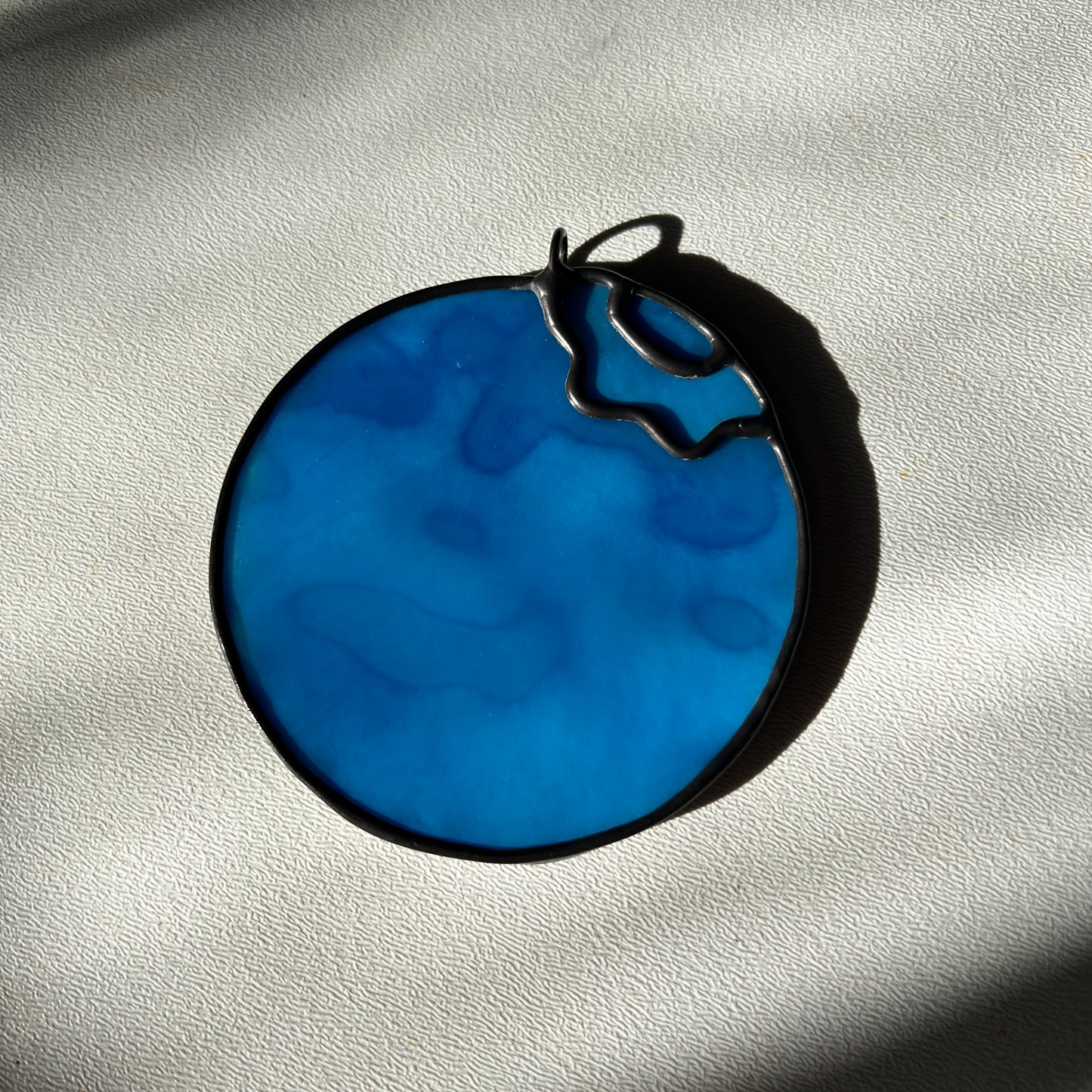 a light blue mottled stained glass blueberry resting on a white surface