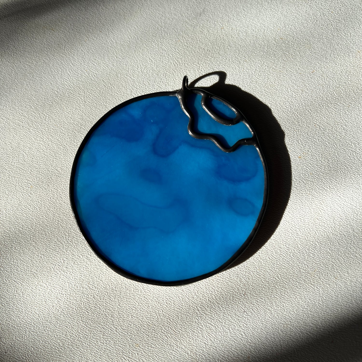 a light blue mottled stained glass blueberry resting on a white surface