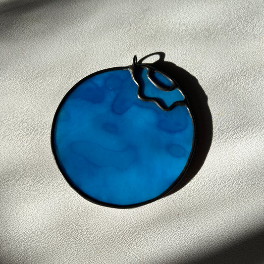 a light blue mottled stained glass blueberry resting on a white surface