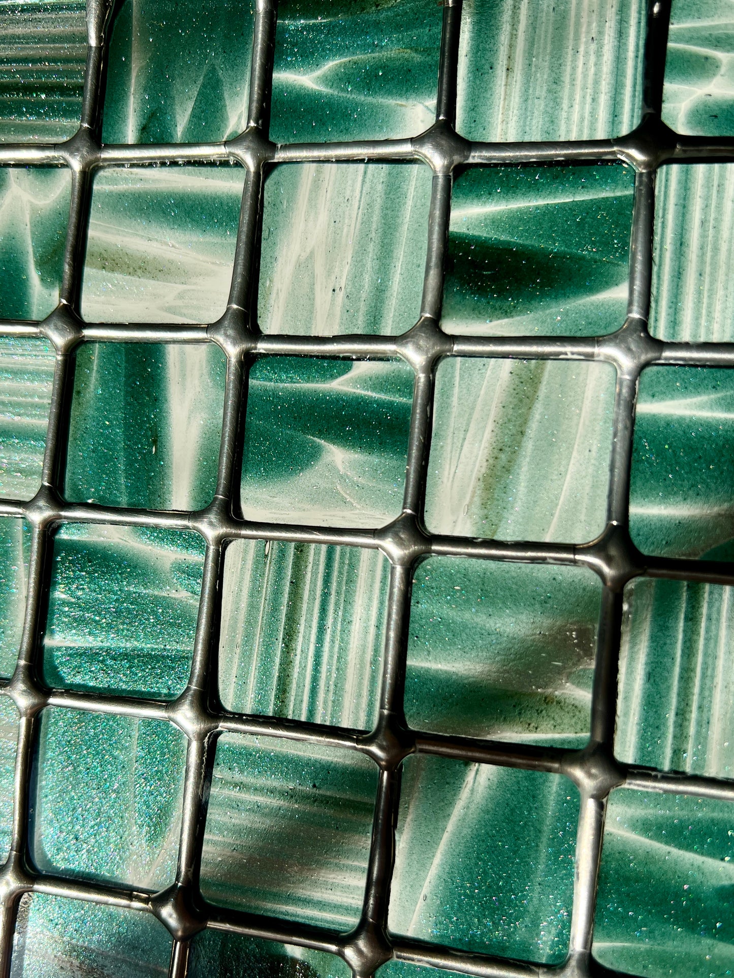 close up of a grid design stained glass panel with striped and mottled sparkly clear and teal glass 