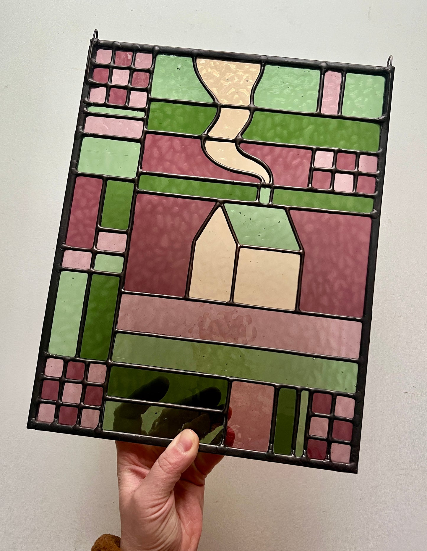 Stained glass panel with geometric design held by a hand against a white background