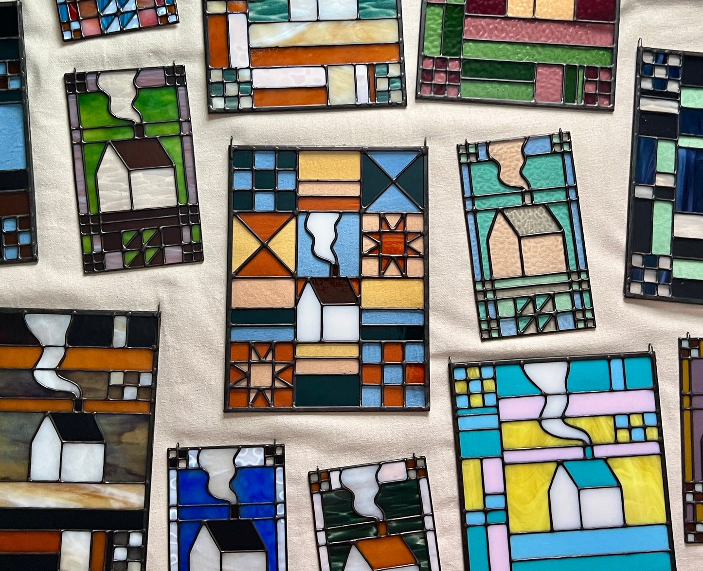 Flat lay of several textile inspired stained glass panels in varying color combinations against a beige backdrop