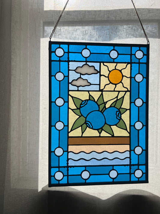 stained glass panel with a simple compartment style design featuring clouds, sun, water, and a small bunch of blueberries in the middle with a blue border