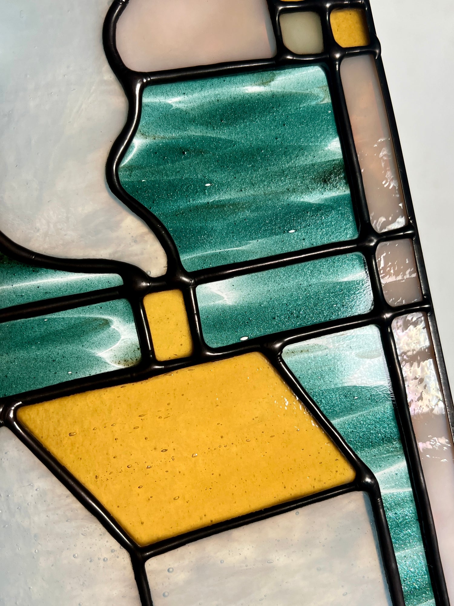 Close up of a stained glass panel, highlighting rich amber and glittery teal glass and smooth solder lines.