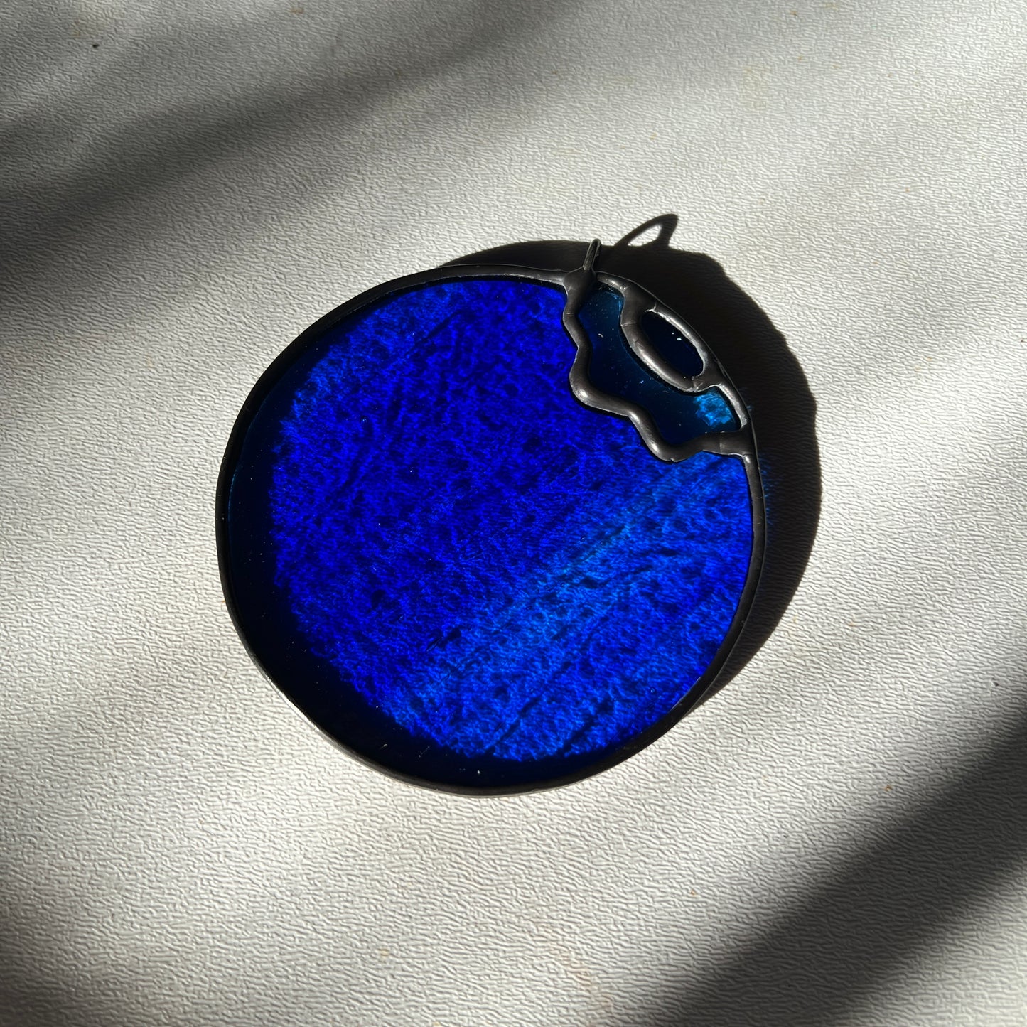 a blue wispy stained glass blueberry resting on a white surface