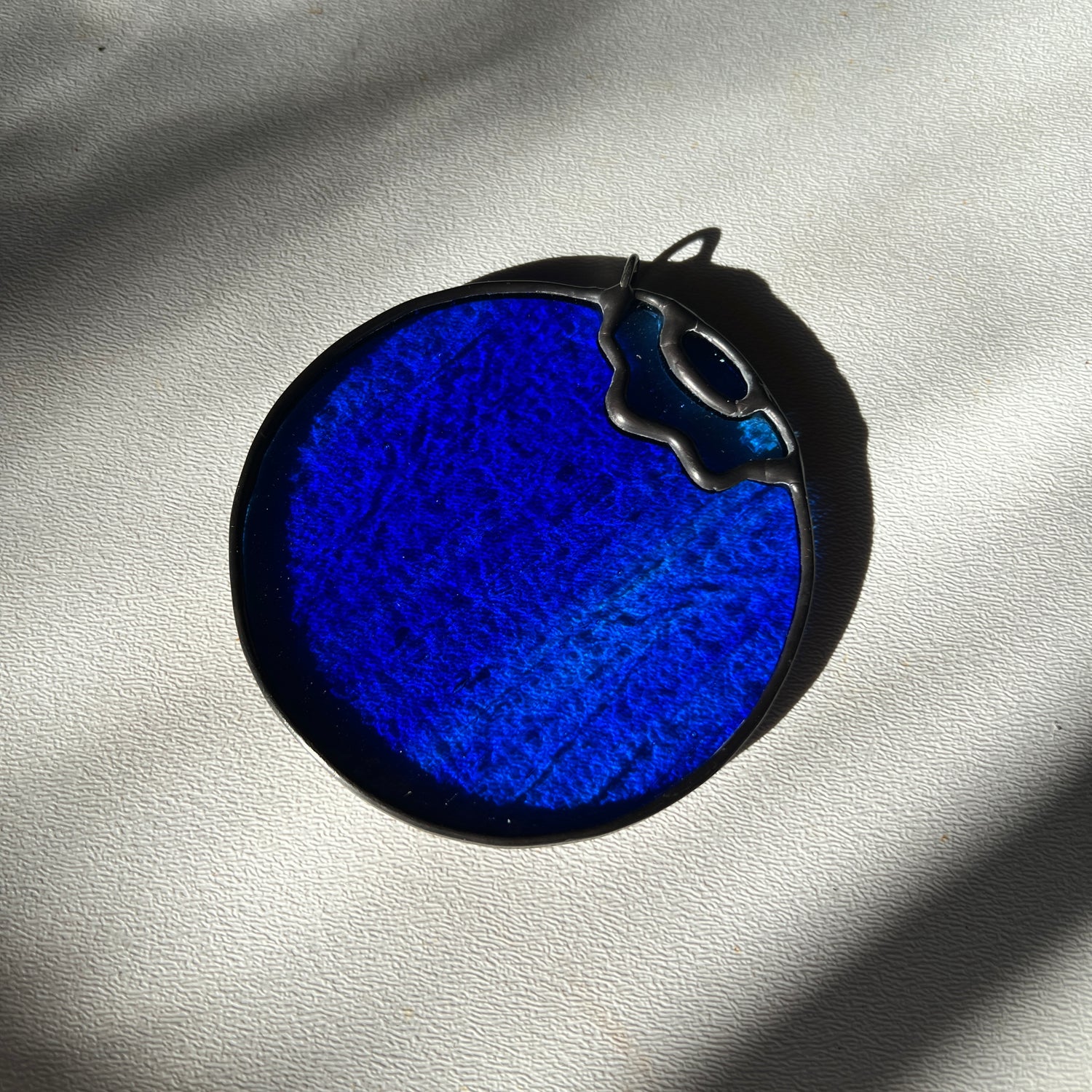 a blue wispy stained glass blueberry resting on a white surface