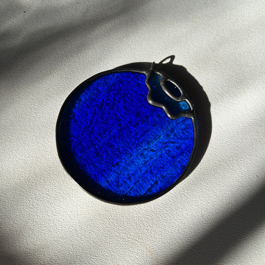 a blue wispy stained glass blueberry resting on a white surface