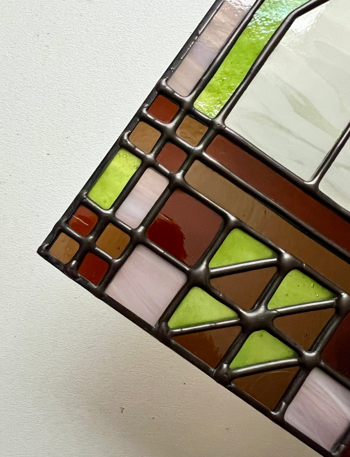 Close up of a textile inspired stained glass panel, focusing on smooth solder lines in a black finish, held above a white background