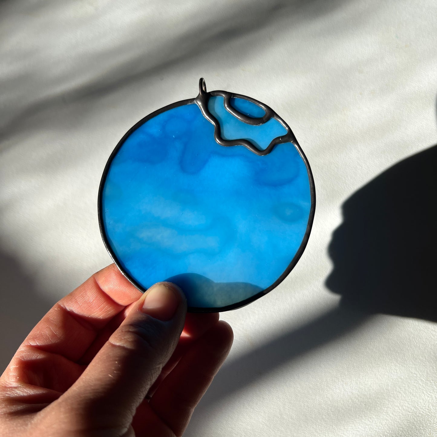 hand holding a light blue mottled stained glass blueberry