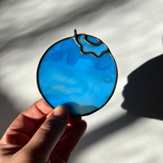 hand holding a light blue mottled stained glass blueberry