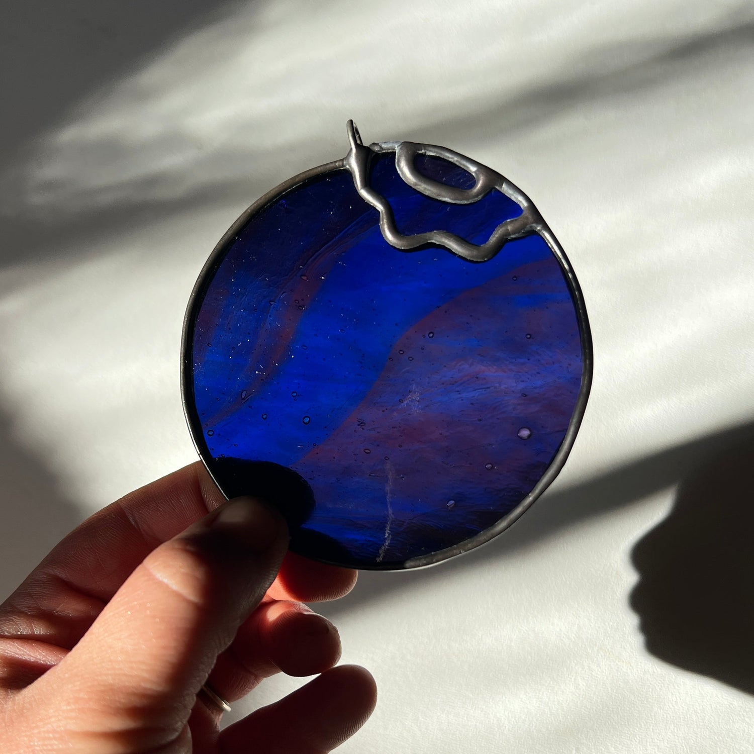 hand holding a wispy deep blue and magenta stained glass blueberry