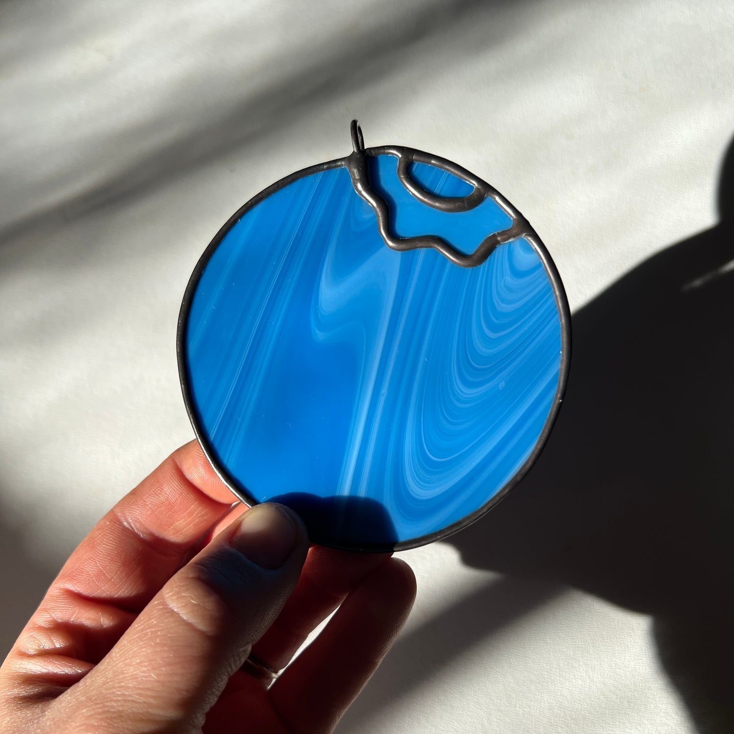 a hand holding a small streaky blue blueberry suncatcher