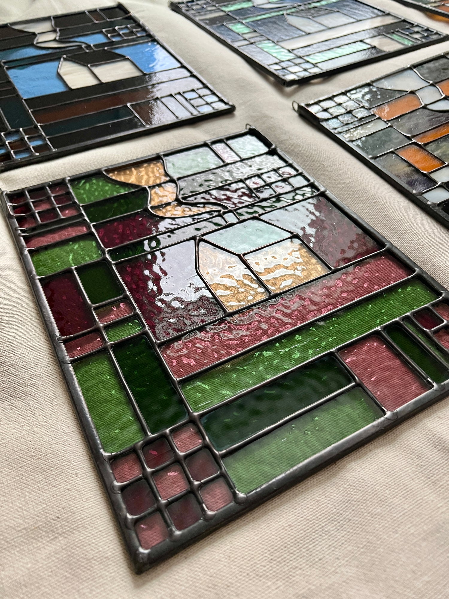 Stained glass textile inspired panels with various colors and designs on a beige surface, shot at an angle to show off smooth solder lines