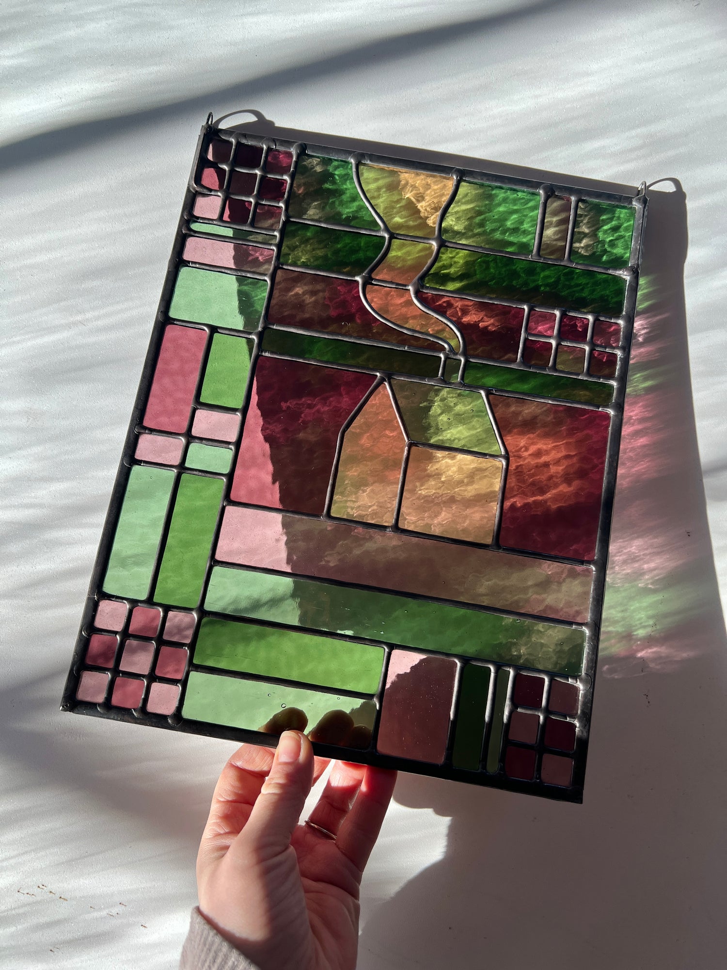 Hand holding a stained glass panel with geometric design on a light background