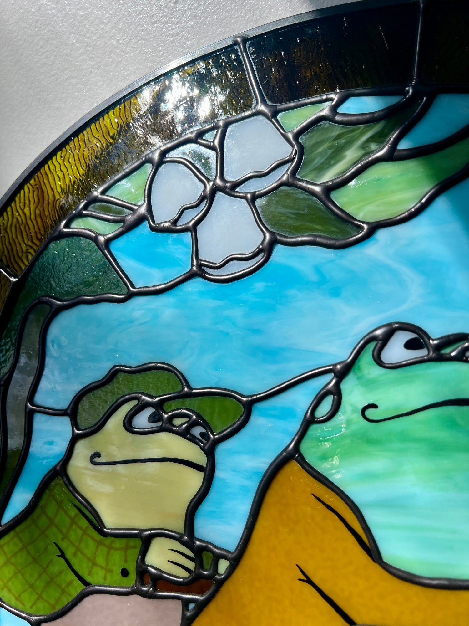 close up of a stained glass panel depicting frog and toad riding a bicycle 