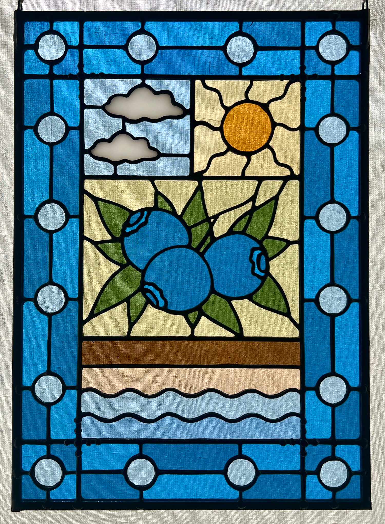 stained glass panel with a simple compartment style design featuring clouds, sun, water, and a small bunch of blueberries in the middle with a blue border