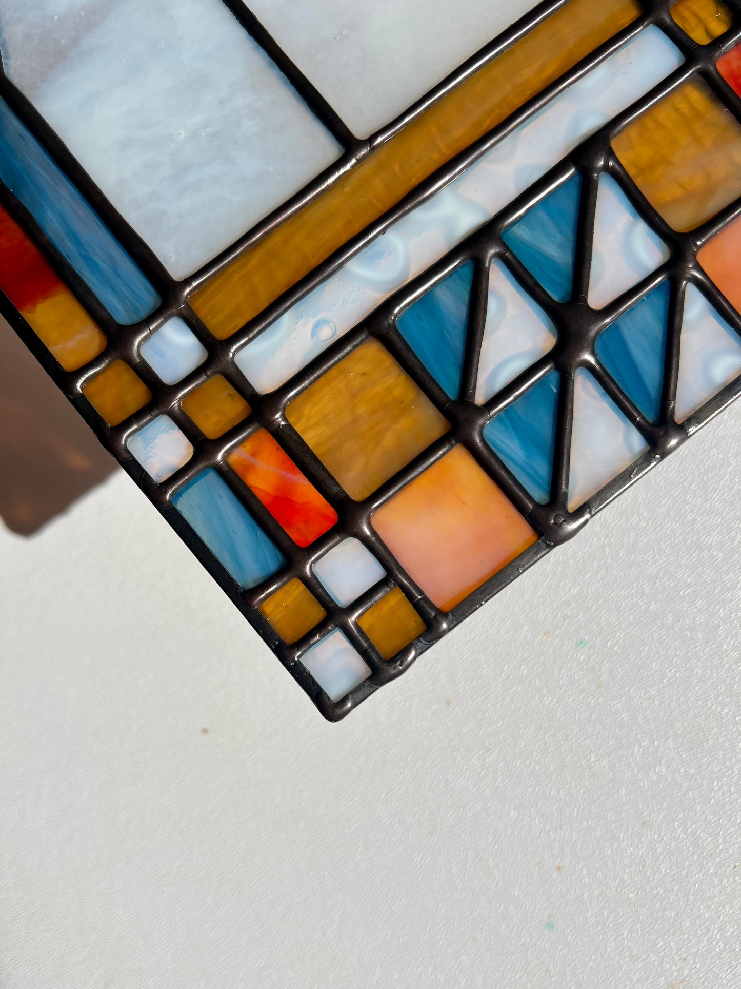 Close up of a stained glass panel against a white background, depicting smooth solder lines and glass in shades of blue, amber, red, and white