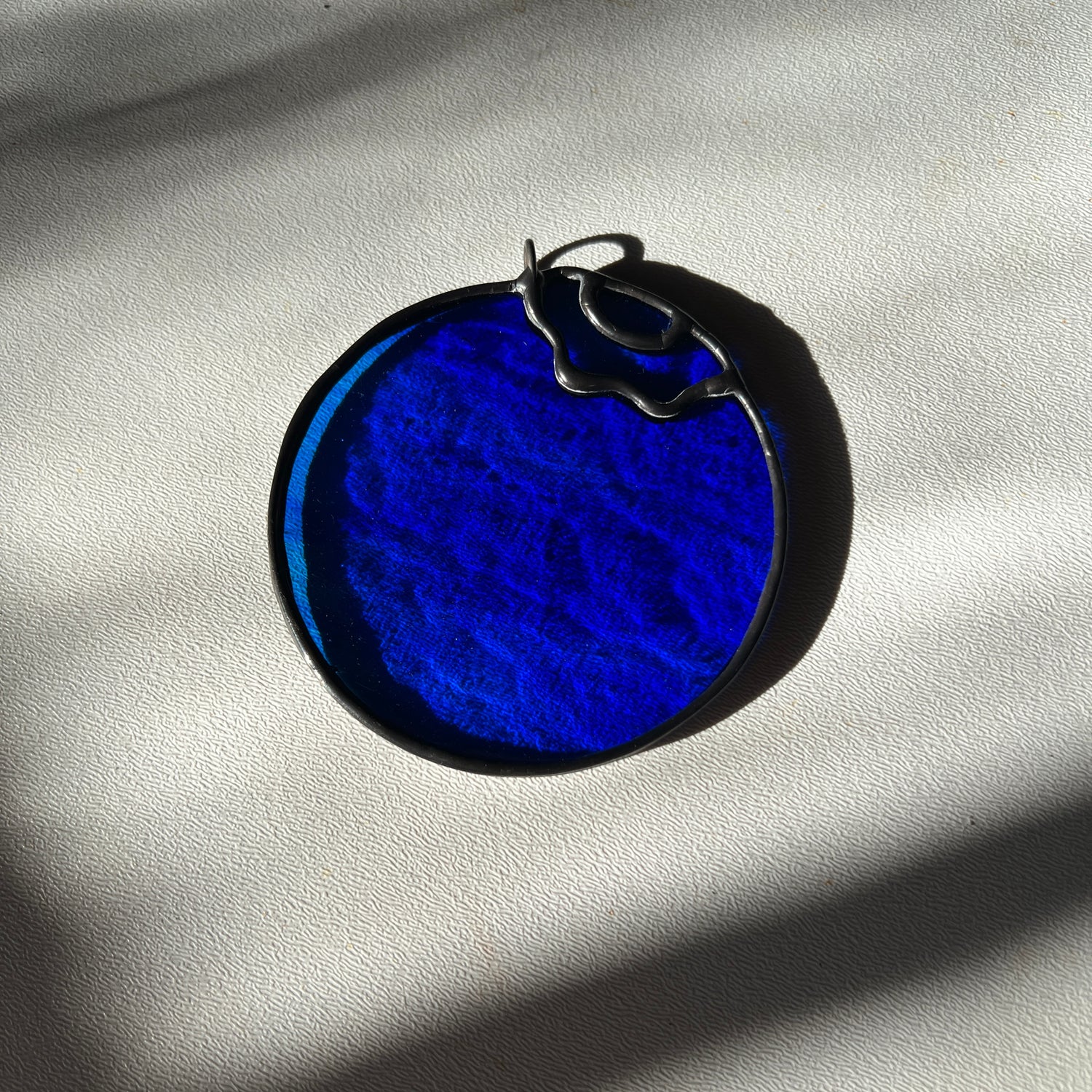 a wispy blue stained glass blueberry resting on a white surface