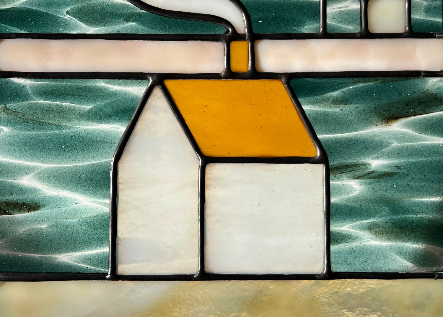 Close up of a stained glass textile inspired panel depicting a home in the center in shades of teal, amber, white, and beige