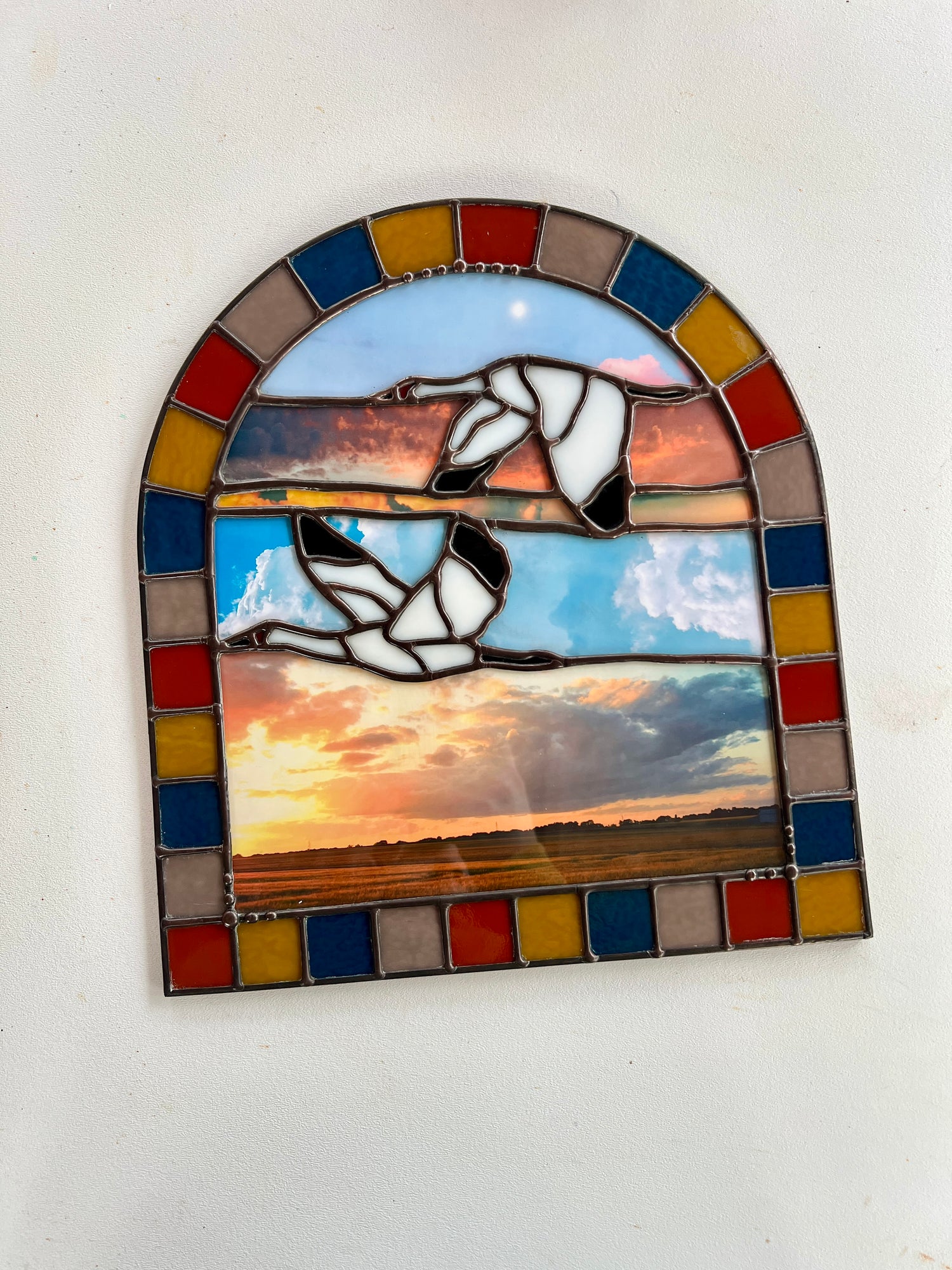 Stained glass panel with a landscape design created by collaged photographs and two cranes flying against a white background