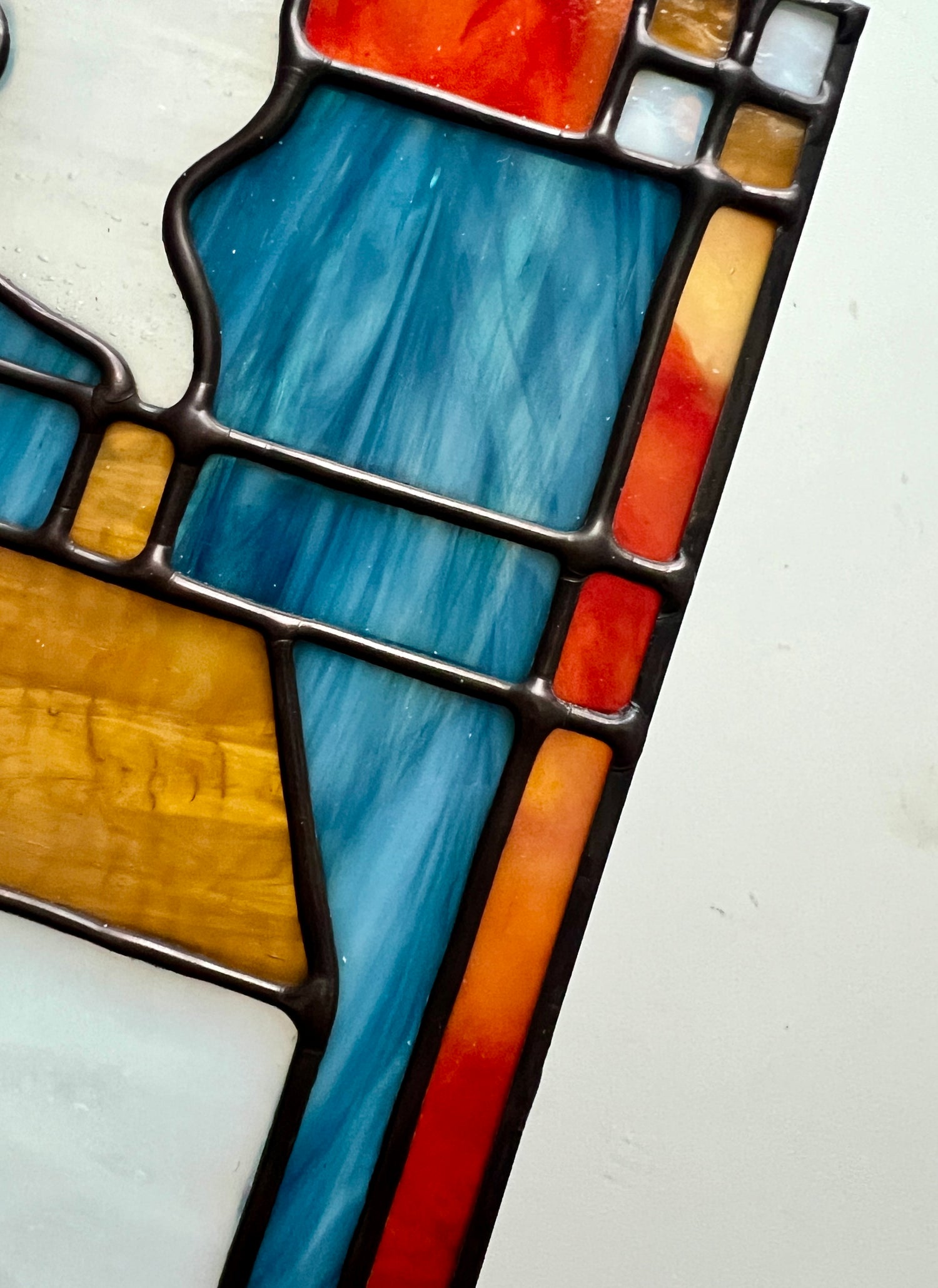 Close up of a stained glass panel, depicting smooth solder lines and wispy blue and red glass