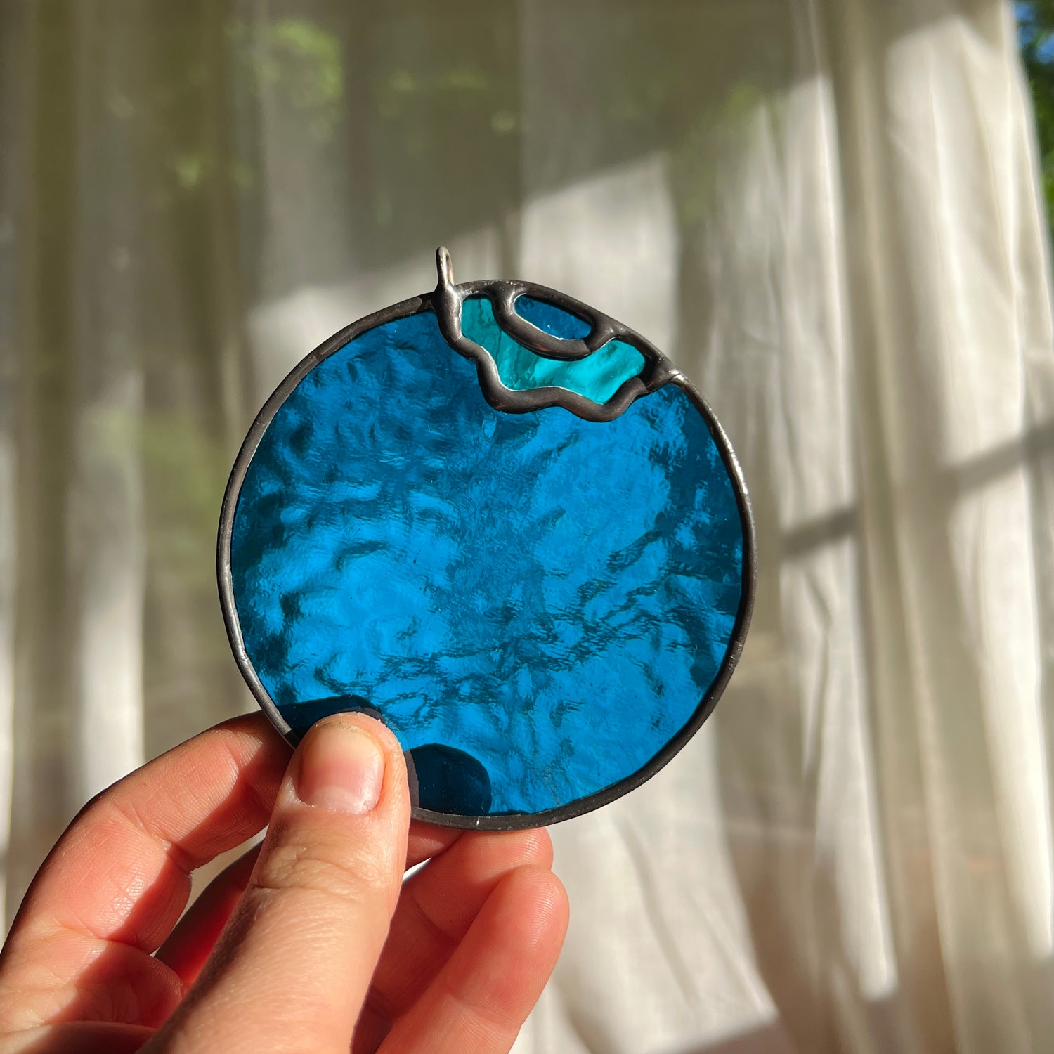hand holding a textured stained glass blueberry in front of a window