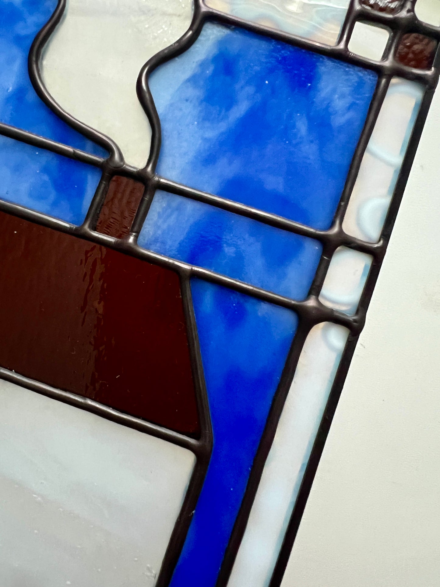 Close up of a stained glass panel highlighting bright blue and mottled white glass, with smooth solder details