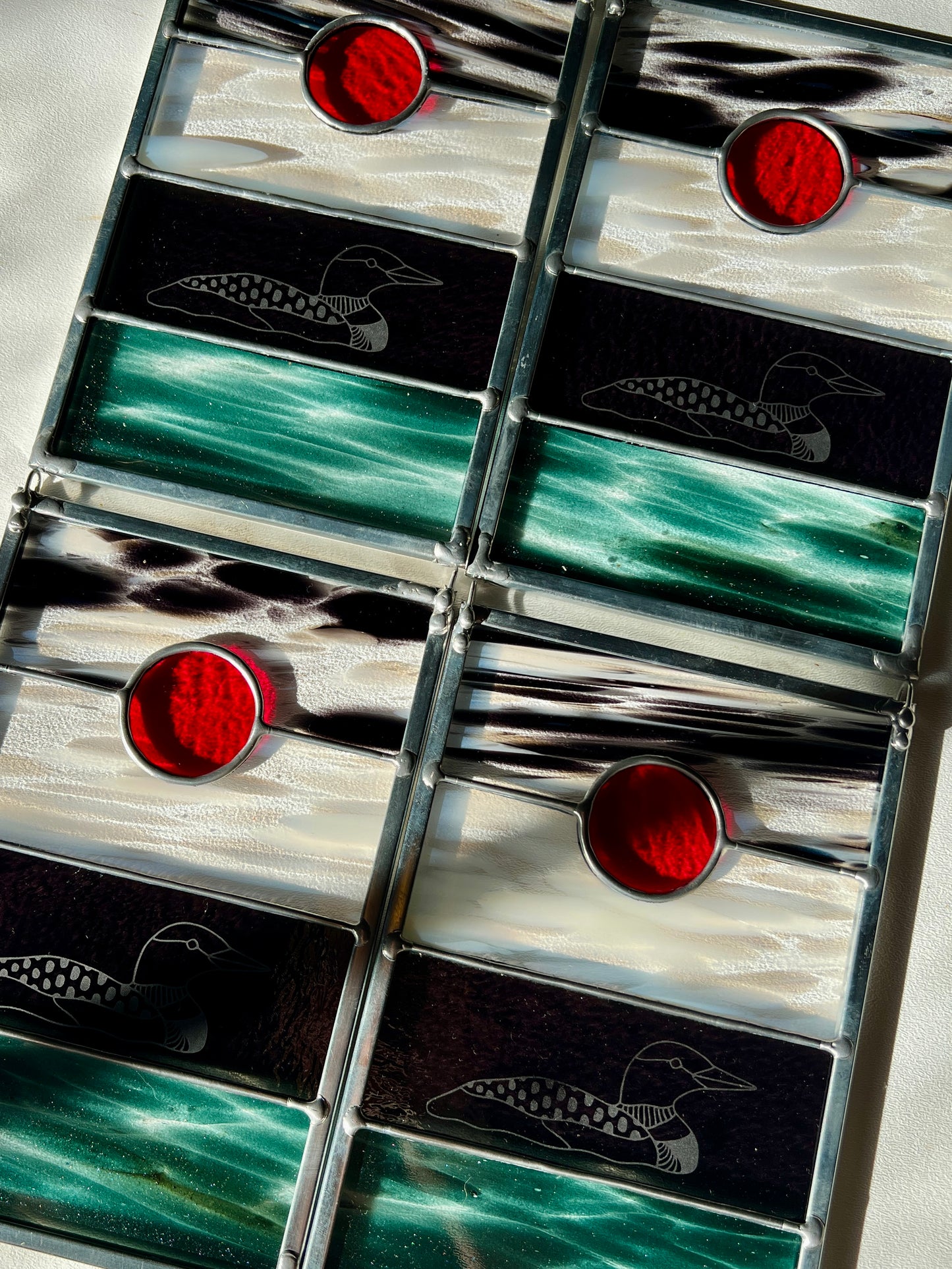 four stained glass panels with black, white, clear, teal, and red glass with loons etched on the surface