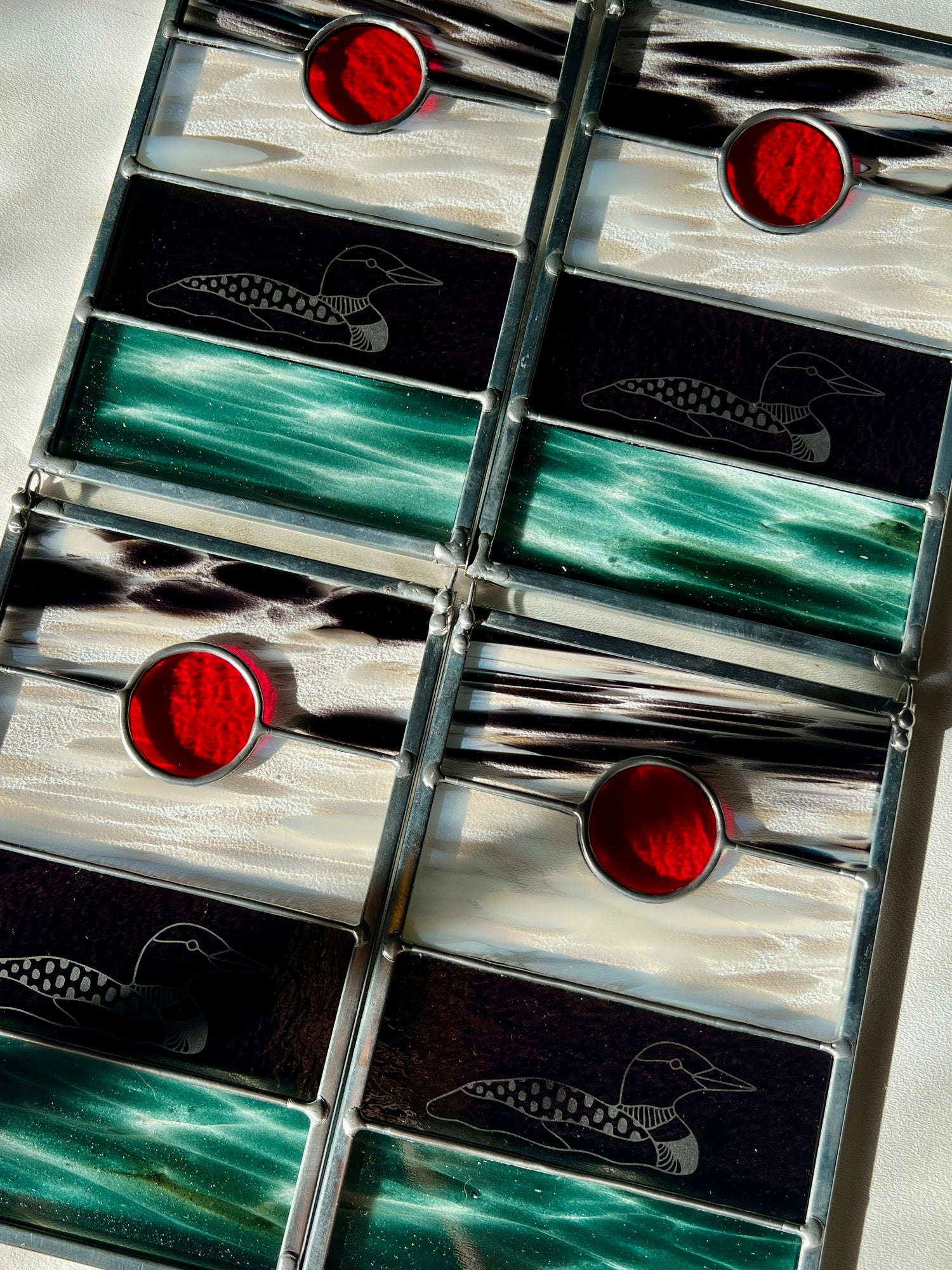 four stained glass panels with black, white, clear, teal, and red glass with loons etched on the surface