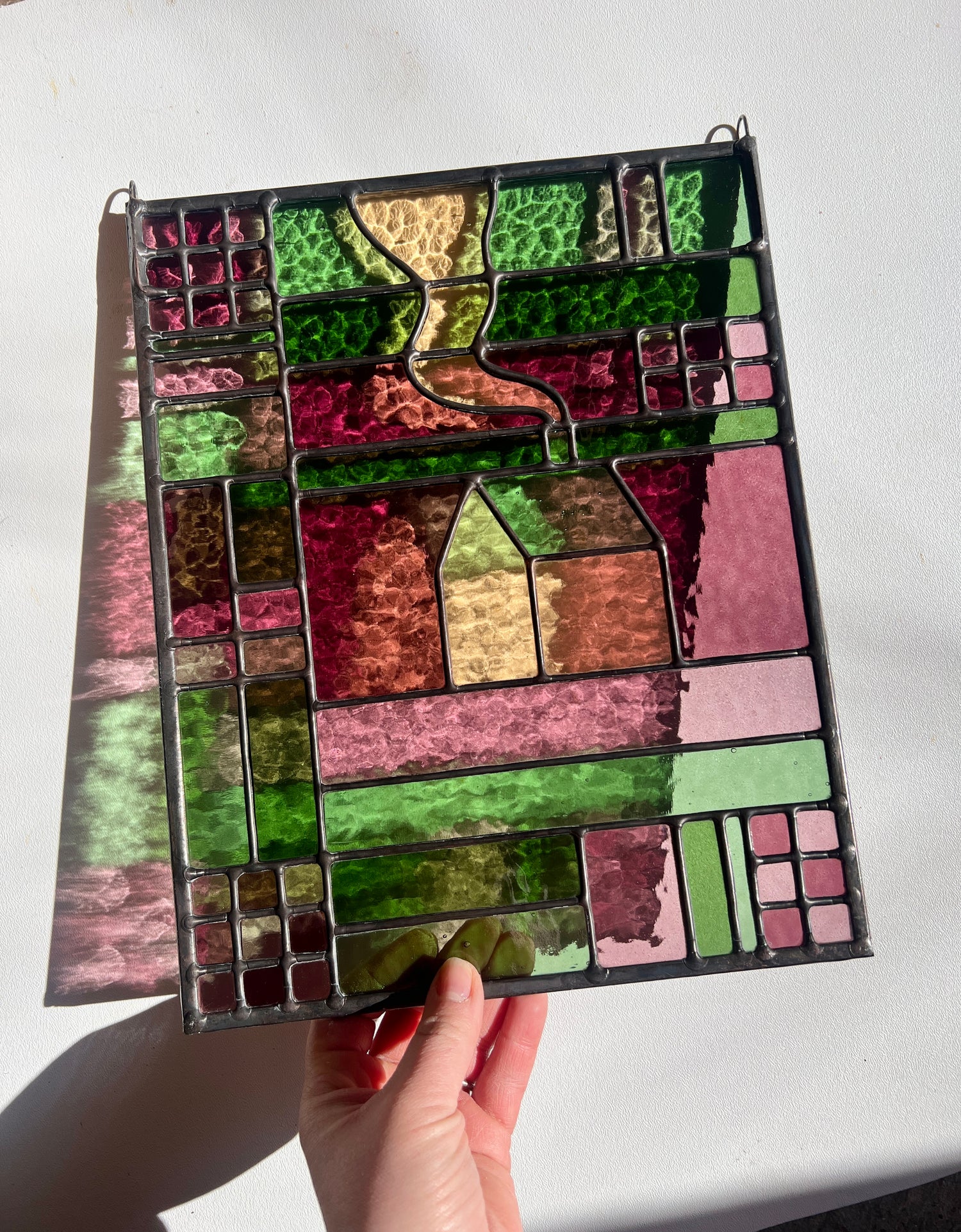 Hand holding a colorful stained glass panel with geometric shapes on a white background