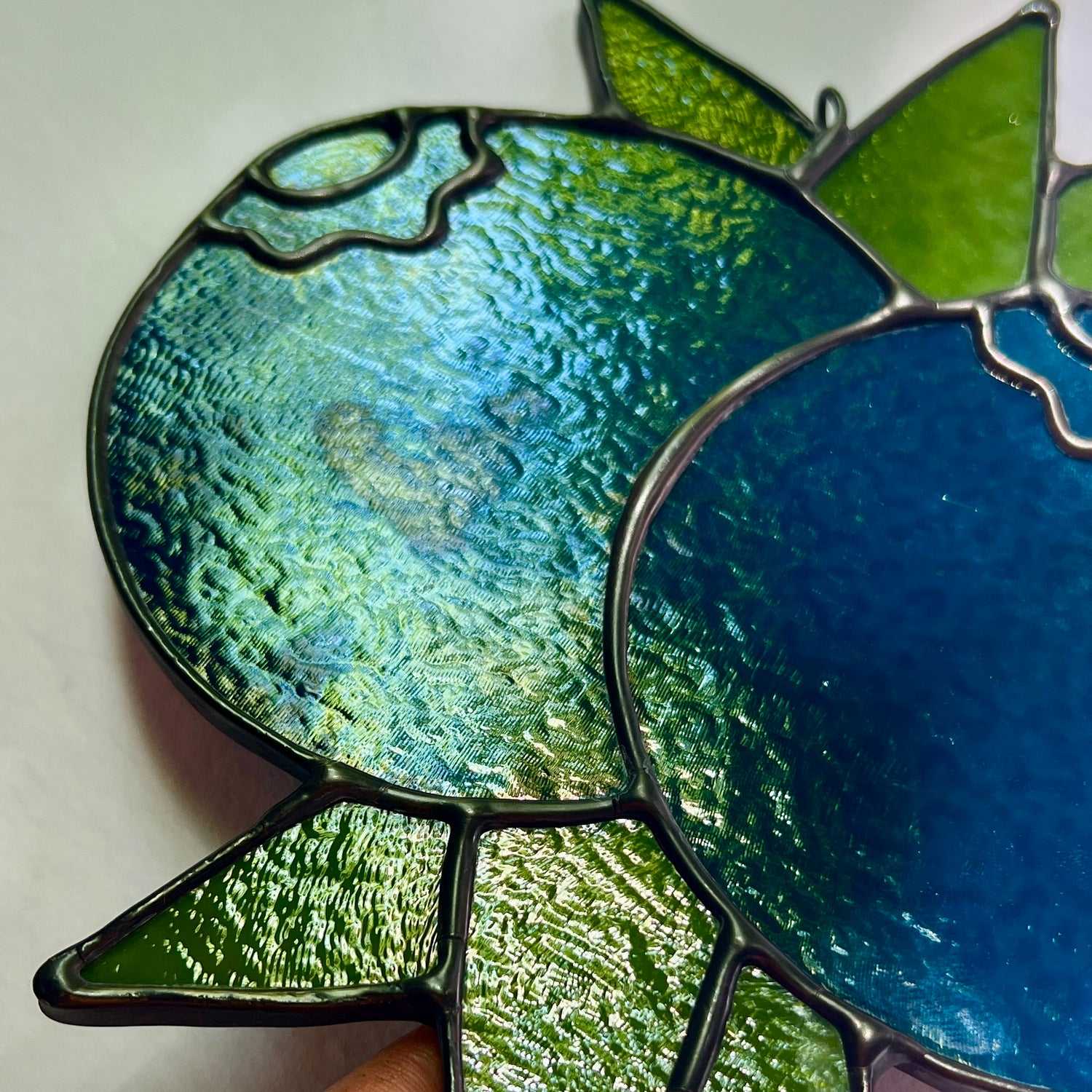 close up of a stained glass blueberry suncatcher showing stains on the surface of the blue glass