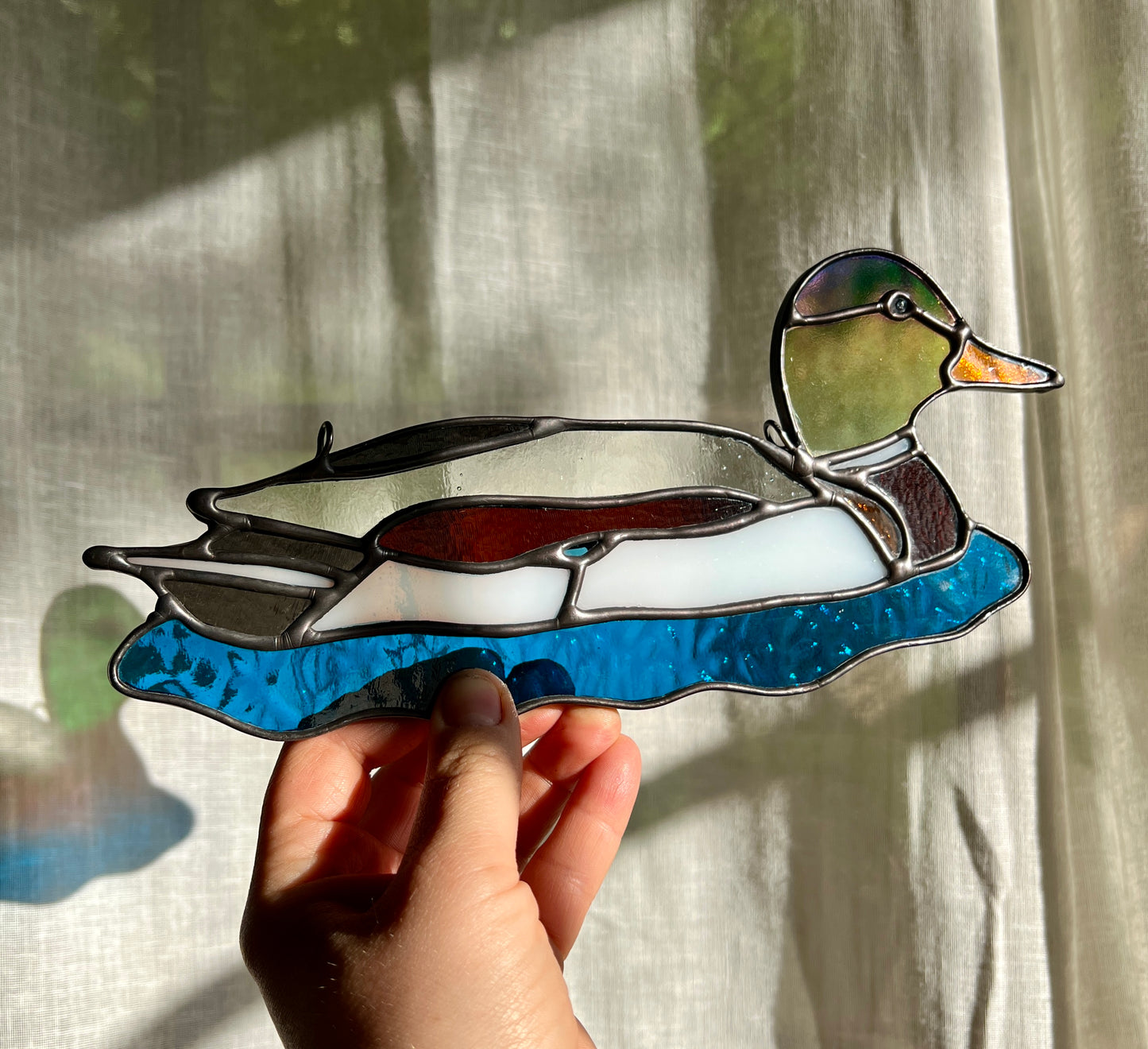 stained glass suncatcher of a male mallard held by a hand at an angle to demonstrate yellow iridescence of the glass used for the head