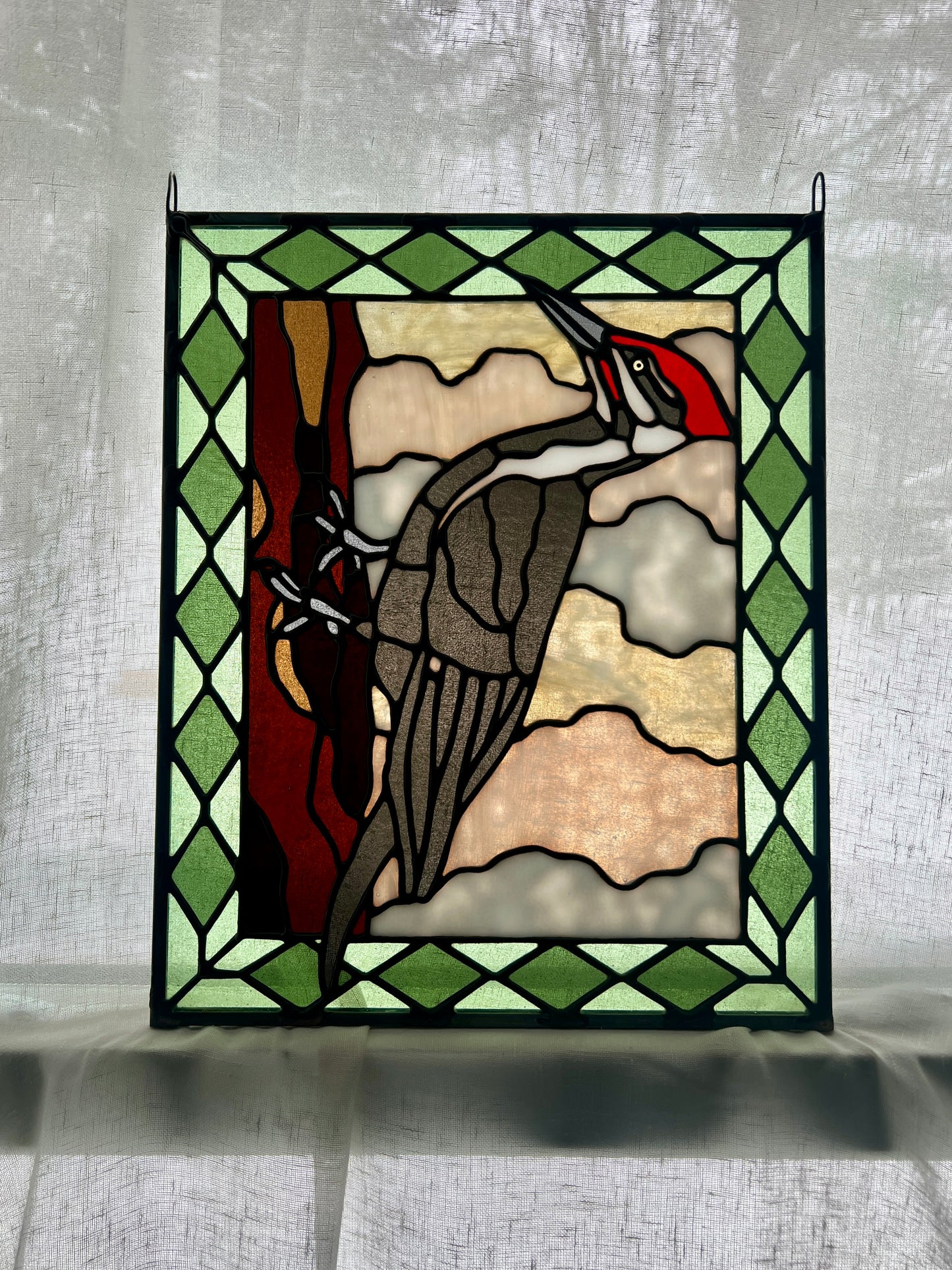 stained glass panel depicting a pileated woodpecker with a green diamond pattern border