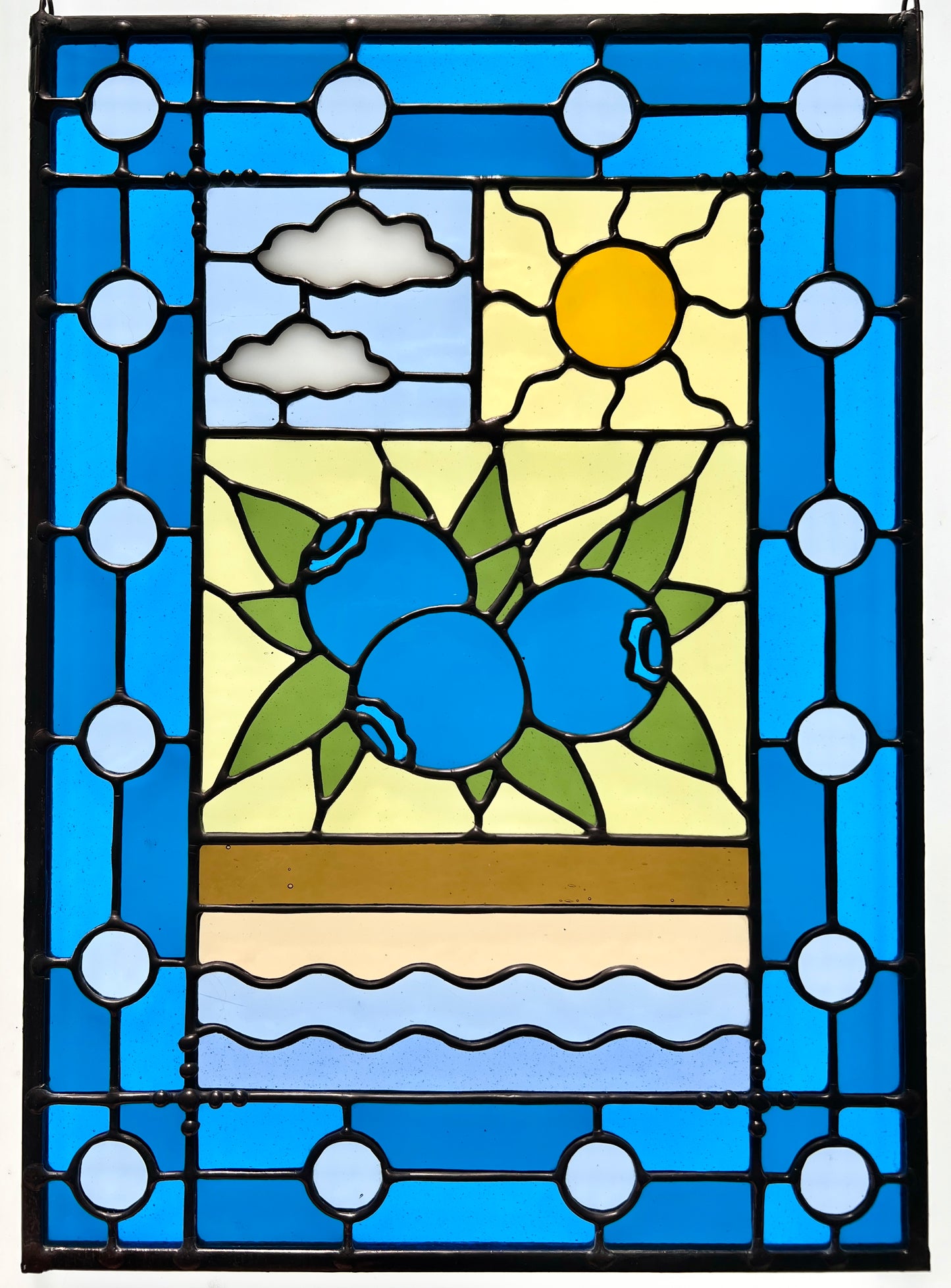 stained glass panel with a simple compartment style design featuring clouds, sun, water, and a small bunch of blueberries in the middle with a blue border