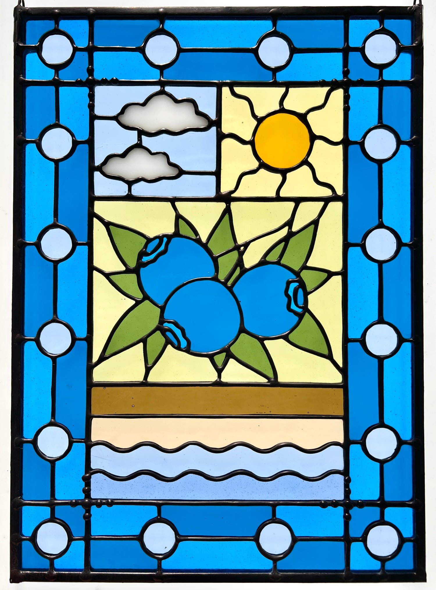stained glass panel with a simple compartment style design featuring clouds, sun, water, and a small bunch of blueberries in the middle with a blue border