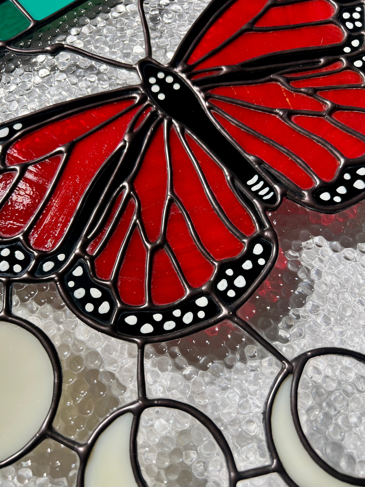 Close up of the hand painted and solder details of a monarch butterfly, part of a larger stained glass panel.