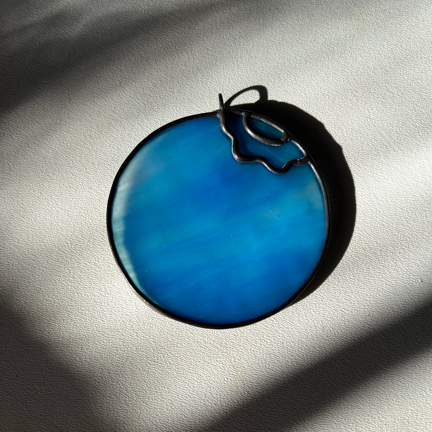  a light blue wispy stained glass blueberry resting on a white surface