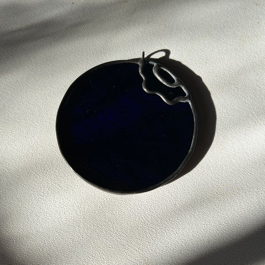 a very deep blue, almost black, stained glass blueberry resting on a white surface