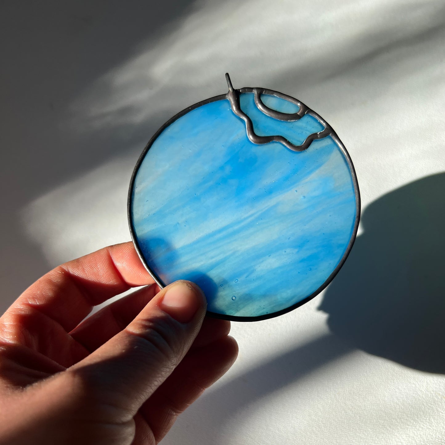 hand holding a light blue wispy stained glass blueberry