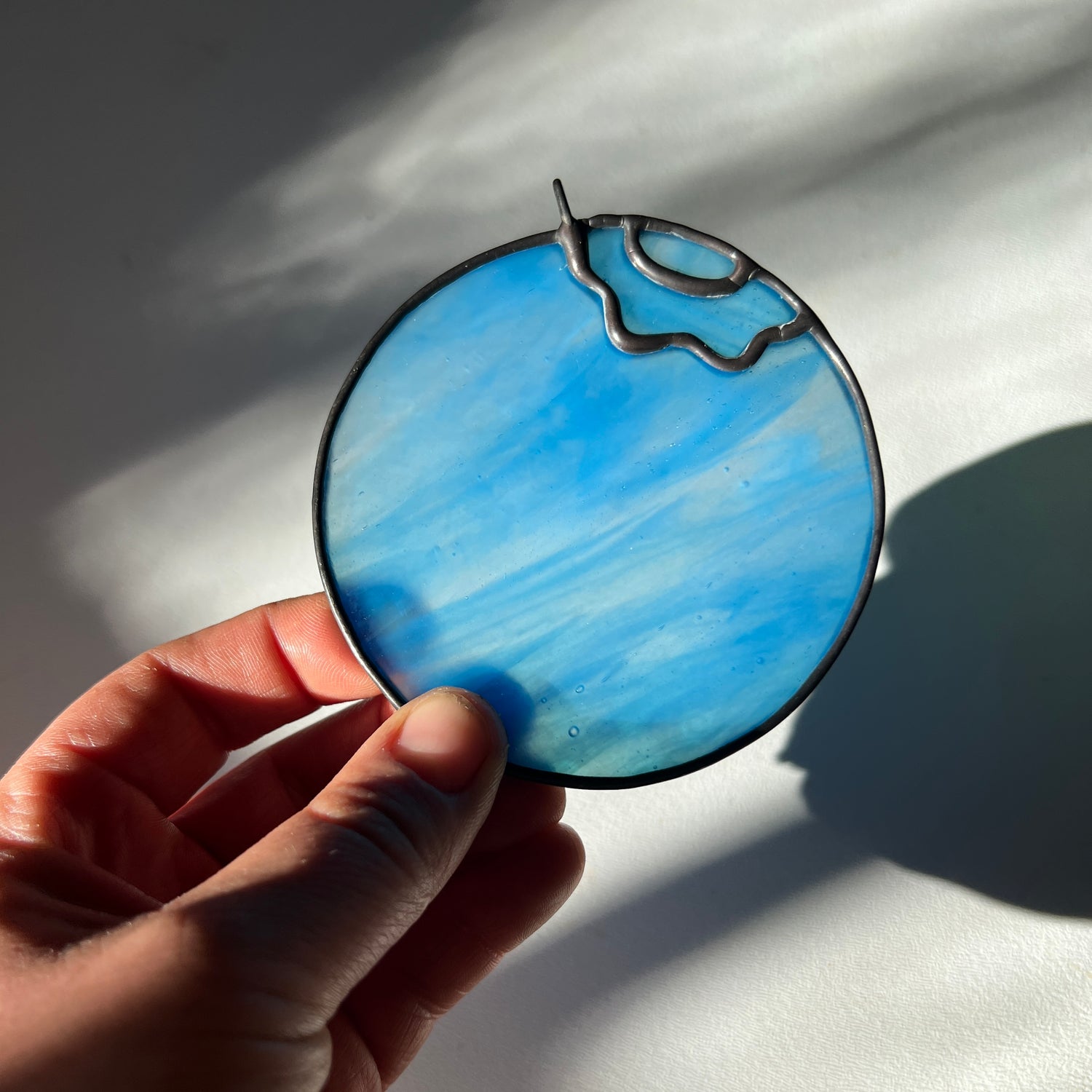 hand holding a light blue wispy stained glass blueberry