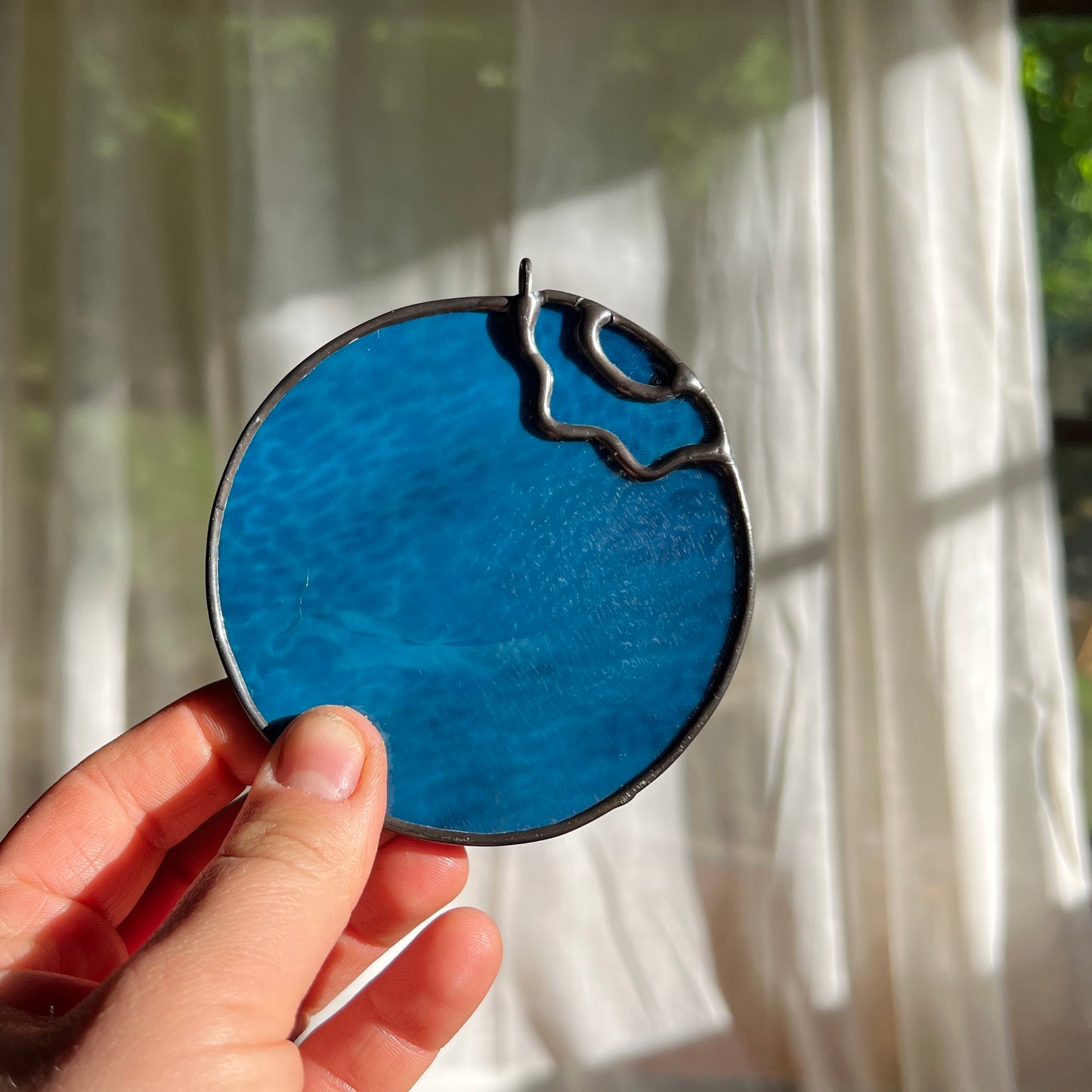 hand holding a stained glass blueberry in front of a window