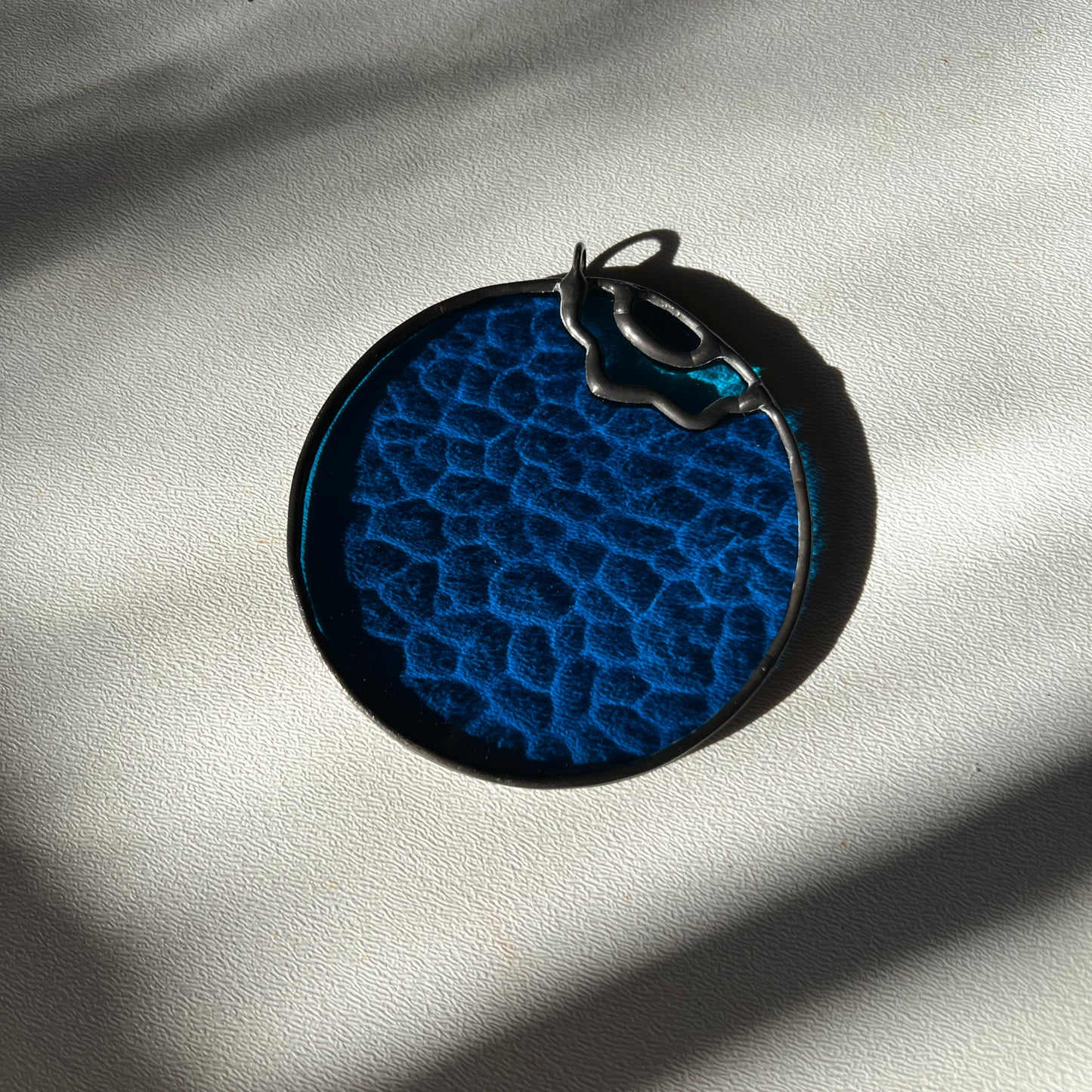 a textured stained glass blueberry resting on a white surface
