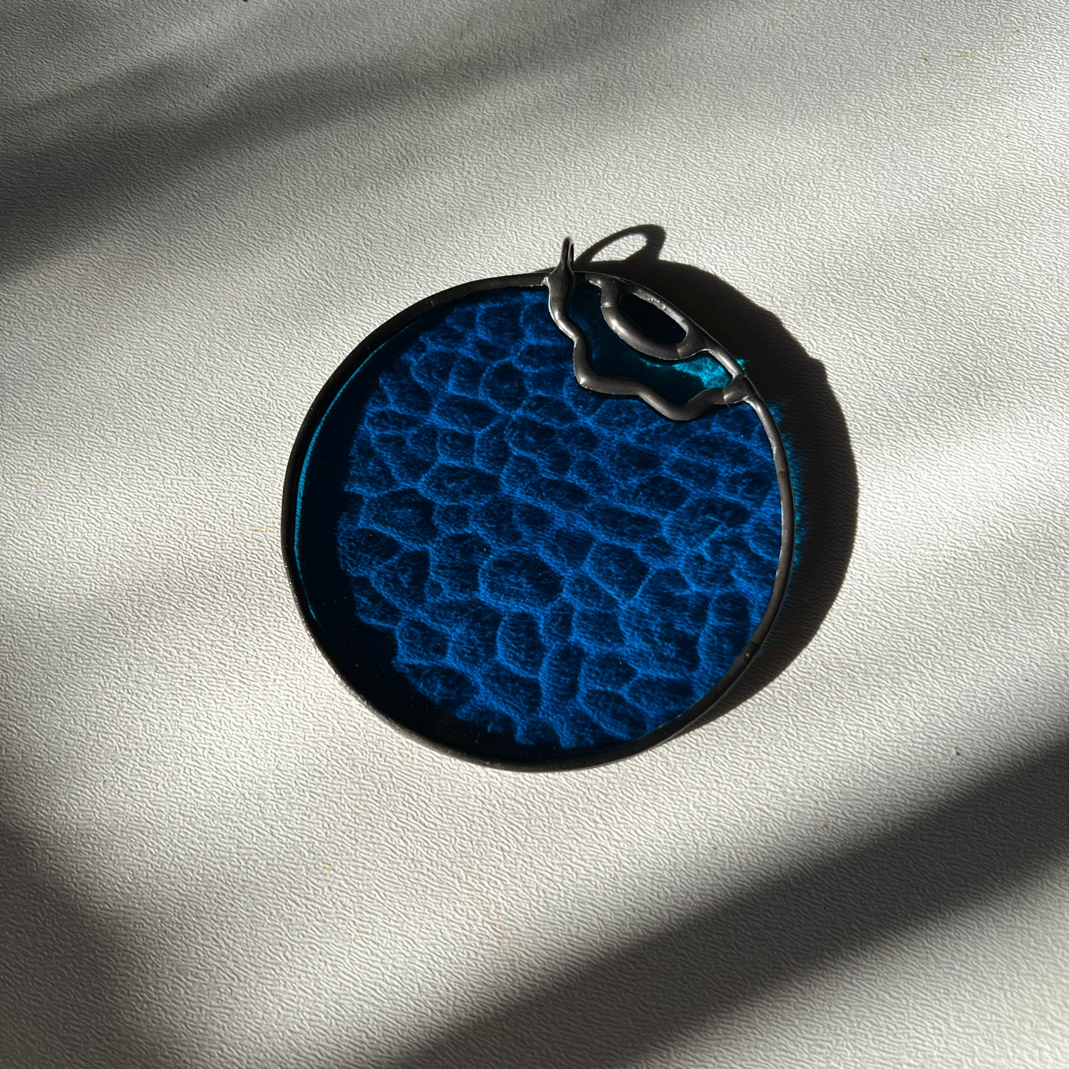 a textured stained glass blueberry resting on a white surface