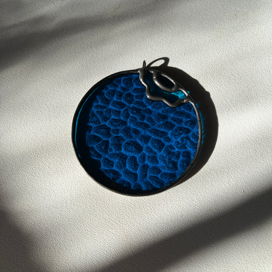 a textured stained glass blueberry resting on a white surface