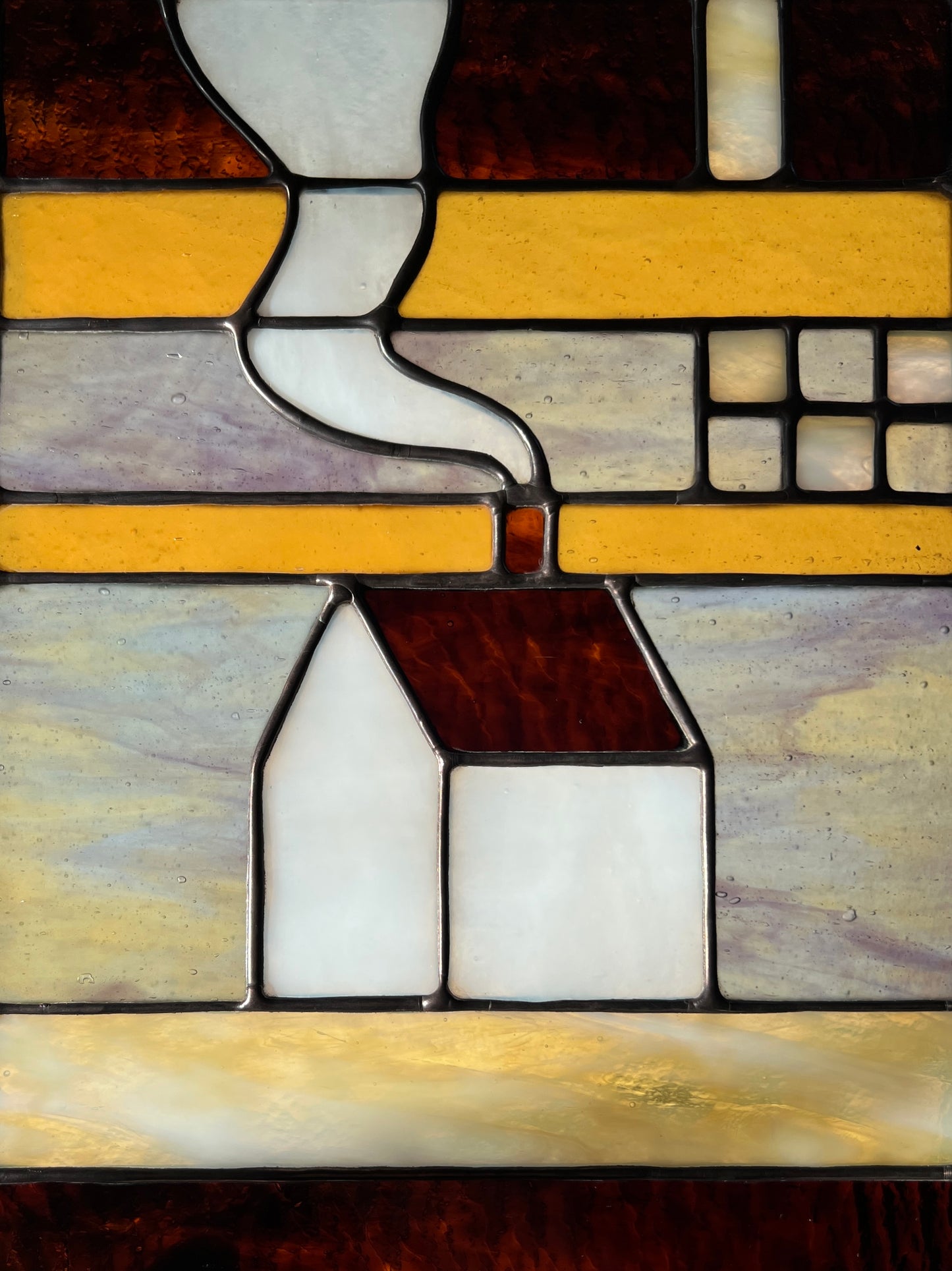 Close up of a stained glass textile inspired panel depicting a home in the center in shades of purple, white, brown, and amber.