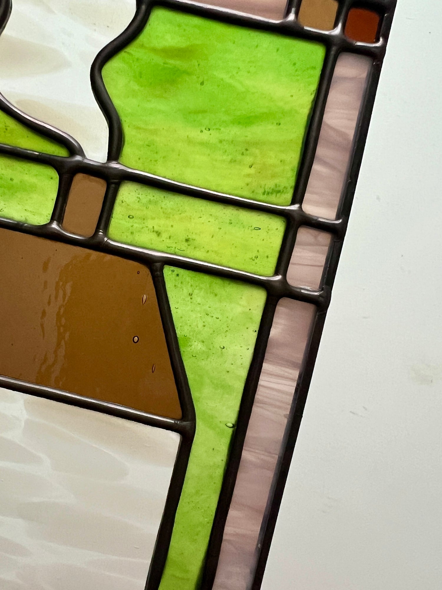 Close-up of a stained glass panel with green and brown colors on a white background