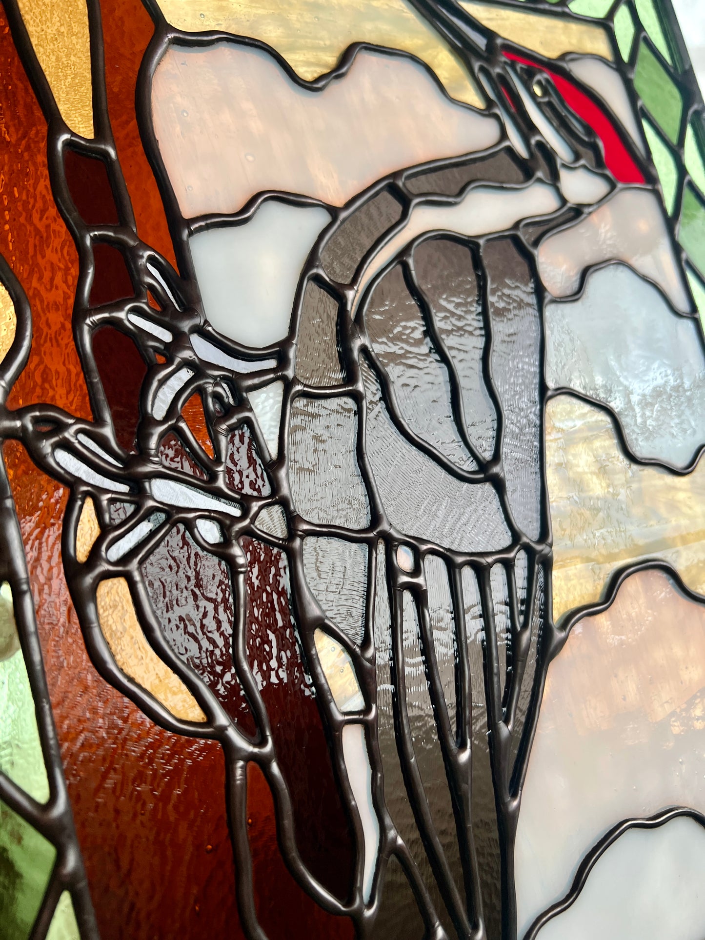 close up view of a stained glass panel depicting a pileated woodpecker with a green diamond pattern border