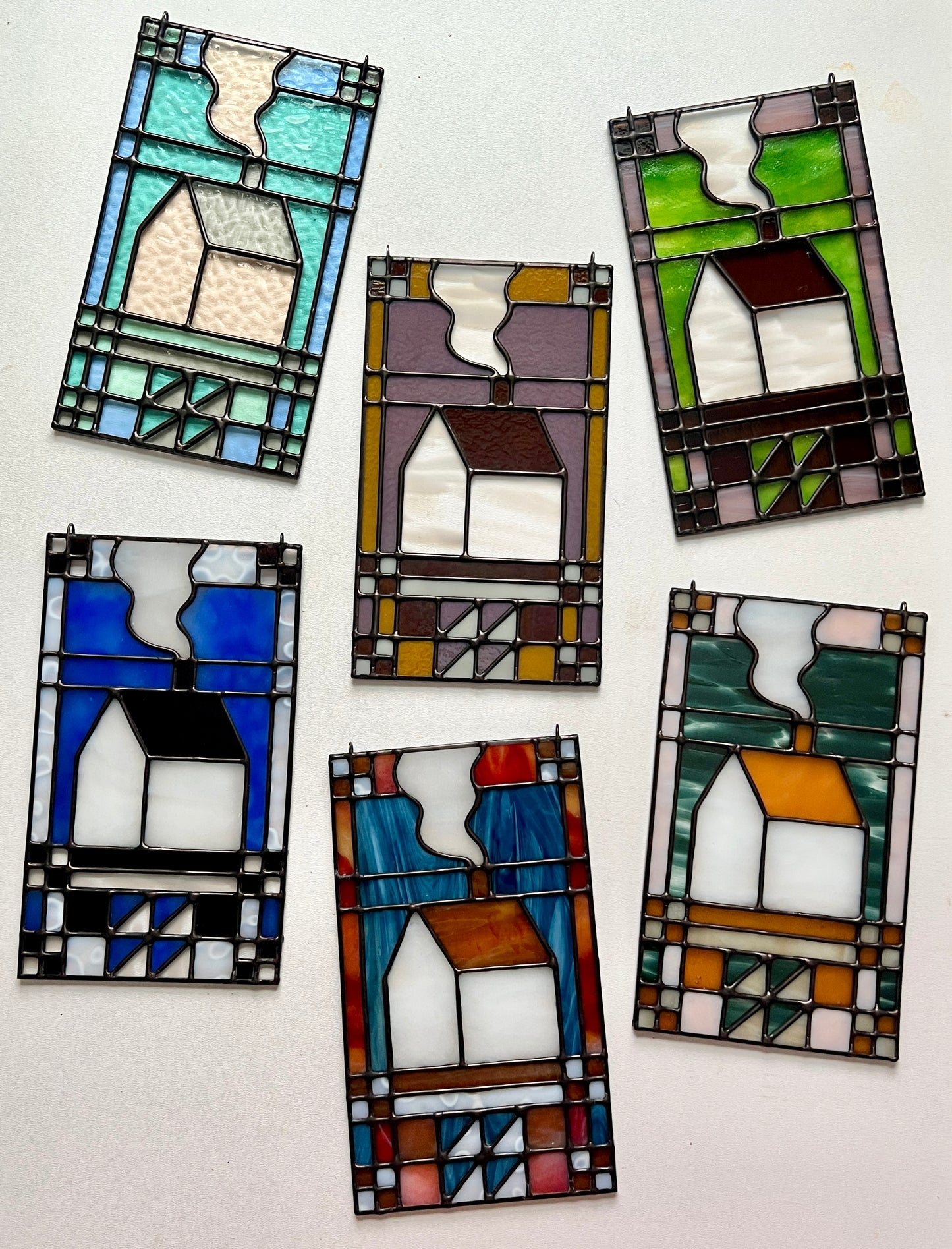 Set of six textile inspired stained glass panels in various color combinations, spread out across a white surface